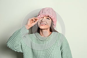 Young woman wearing warm sweater and hat on light background. Winter season