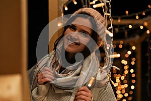 Young woman wearing warm sweater, hat and scarf at night. Winter season