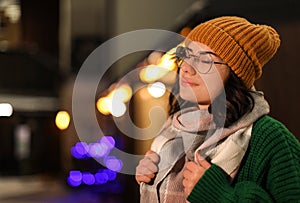 Young woman wearing warm sweater, hat and scarf  at night. Winter season