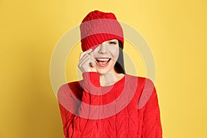 Young woman wearing warm sweater and hat on yellow background. Winter season