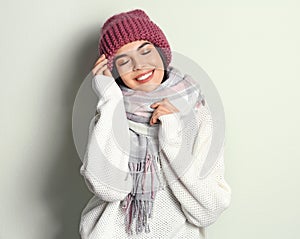 Young woman wearing warm sweater, scarf and hat on light background. Winter season