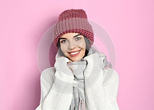 Young woman wearing warm sweater, scarf and hat on pink background. Winter season