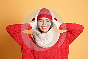 Young woman wearing warm sweater, scarf, mittens and hat on yellow background. Winter season