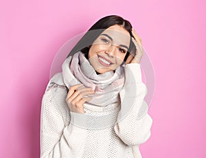 Young woman wearing warm sweater and scarf on pink background. Winter season