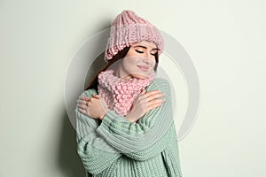 Young woman wearing warm sweater, snood and hat on light background. Winter season