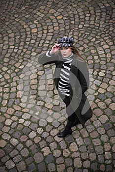 young woman wearing a winter green coat and hat walking on cobblestone in the street