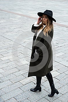 young woman wearing a winter green coat and hat walking  in the street