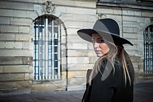 young woman wearing a winter green coat and hat walking  in the street