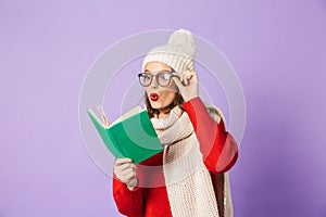 Young woman wearing winter hat isolated over purple background reading book