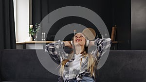 Young woman wearing wireless headphones, listening relaxing music, resting on sofa, enjoying weekend