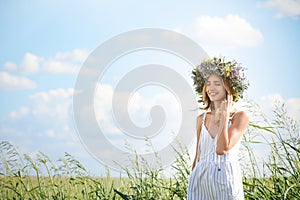 Young woman wearing wreath made of beautiful flowers in field on sunny day