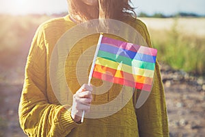 Young woman wearing yellow sweater holding lgbt rainbow flag outside, same sex couples, freedom, love,