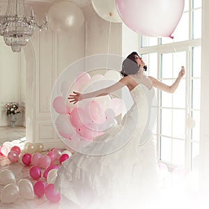 Young woman in wedding dress in luxury interior flies on pink and white balloons.