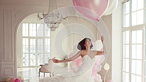 Young woman in wedding dress in luxury interior flies on pink and white balloons.