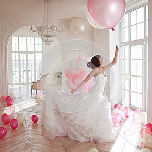 Young woman in wedding dress in luxury interior flies on pink and white balloons.