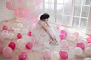 Young woman in wedding dress in luxury interior with a mass of pink and white balloons. Hold in hands her white shoes