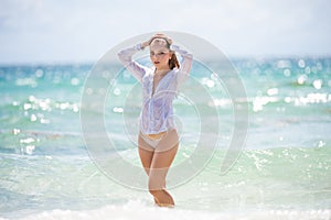 Young woman in wet sexy dress on tropical beach. Beautiful girl on summer vacation. Sensual woman in white shirt and