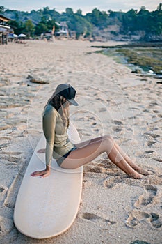 young woman in wetsuit relaxing on surfboard