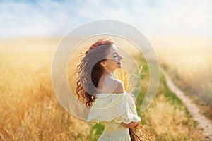 A young woman in a wheat field with ears in her hands, a sunny summer morning