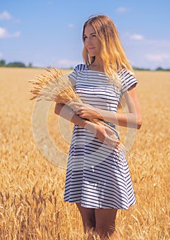 Young woman at the wheat field under the blue sky at the sunny day
