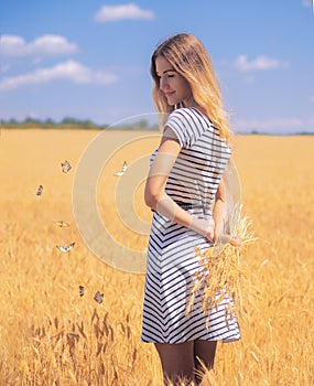 Young woman at the wheat field under the blue sky at the sunny day