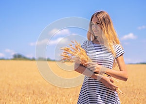 Young woman at the wheat field under the blue sky at the sunny day