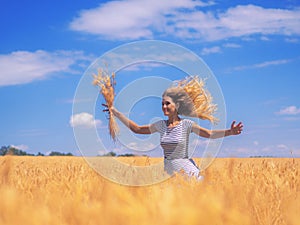 Young woman at the wheat field under the blue sky at the sunny day