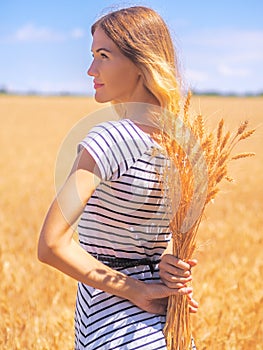 Young woman at the wheat field under the blue sky at the sunny day