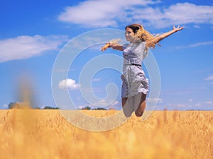 Young woman at the wheat field under the blue sky at the sunny d