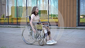 Young woman in a wheelchair. A girl rides in a wheelchair against the background of a glass building. Special transport