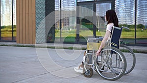 Young woman in a wheelchair. A girl rides in a wheelchair against the background of a glass building. Special transport