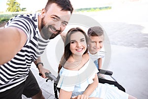 Young woman in wheelchair with her family taking selfie outdoors