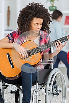 Young woman in wheelchair playing guitar at home