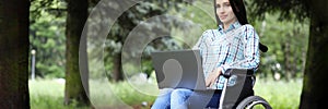 Young woman in wheelchair working on laptop in park