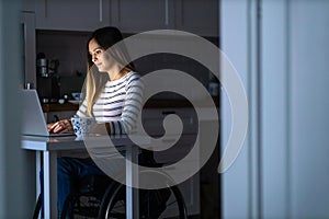 Young woman in wheelchair working on laptop till late