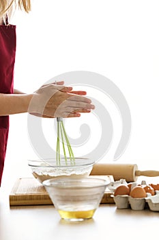 Young woman whisking eggs in glass bowl on kitchen table at home.