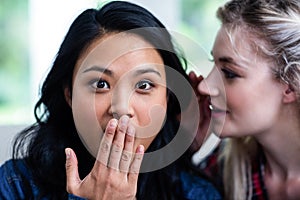 Young woman whispering to surprised female friend