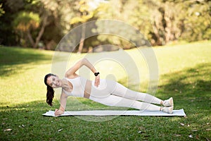 A young woman in white activewear smiles while performing a side plank exercise