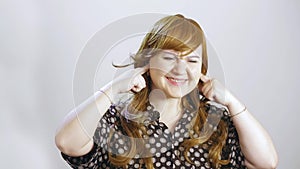 A young woman on a white background pinches her ears and shows her face that she is unpleasant in sound