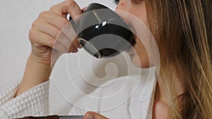 Young woman in white bathrobe enjoying her cup of tea or coffee or chocolate after spa procedure. Female hand brings mug