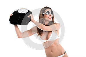 Young woman in white bikini furious hurl weight scale . Fit and healthy concept. Isolated over white background photo