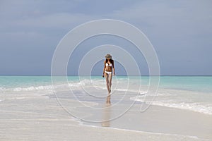 Young woman in white bikini walking on the beach