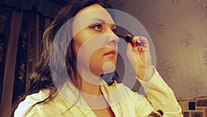 A young woman in a white coat smokes her eyelashes with mascara