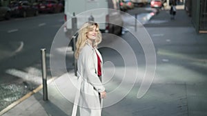 Young woman in white coat walking in the street and waving to camera