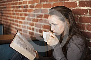 Young Woman with White Coffee Cup Reads Her Bible