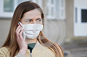 Young woman with white cotton hand made face nose mouth mask talking over her mobile phone, close portrait. Can be used during