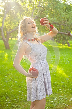 Young woman in white cute polka dot dress walking in an apple garden on a lovely sunny summer day