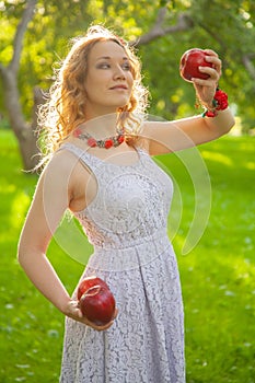Young woman in white cute polka dot dress walking in an apple garden on a lovely sunny summer day