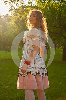 Young woman in white cute polka dot dress walking in an apple garden on a lovely sunny summer day