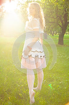 Young woman in white cute polka dot dress walking in an apple garden on a lovely sunny summer day